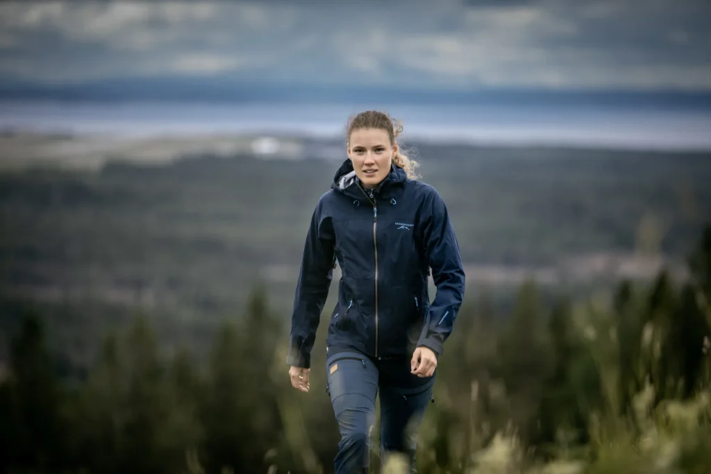 Kvinna i friluftskläder vandrar genom ett grönt landskap