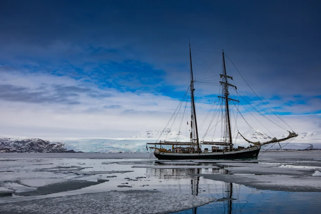 Segelfartyg på stilla vatten framför snötäckta berg och en glaciär på Svalbard